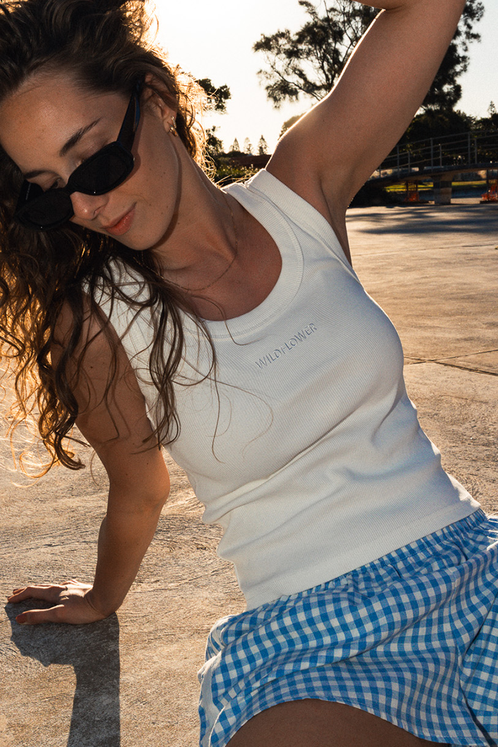 Woman in a white tank top and blue checkered shorts posing outdoors.